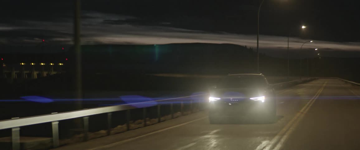 A vehicle driving on a bridge with a mountain range the sky and clouds in the background