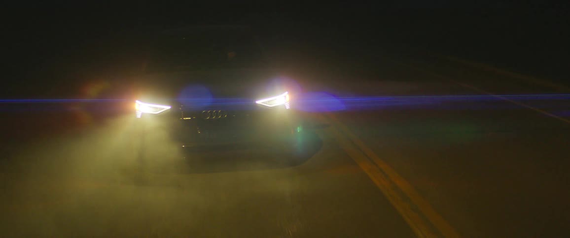 Audi grey car travels on highway illuminating the road with headlights at night