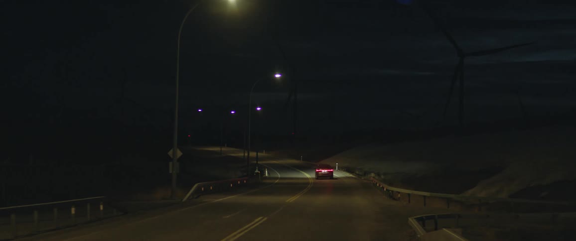 A vehicle driving on a road with wind turbines the sky and clouds in the background