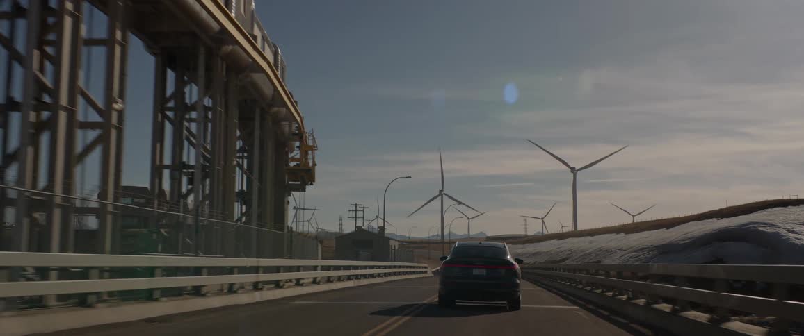 A car is driving around the road past windmills