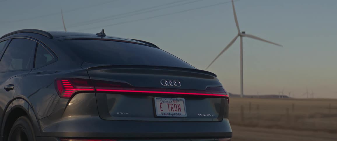 A vehicle driving on a road with wind turbines the sky and clouds in the background
