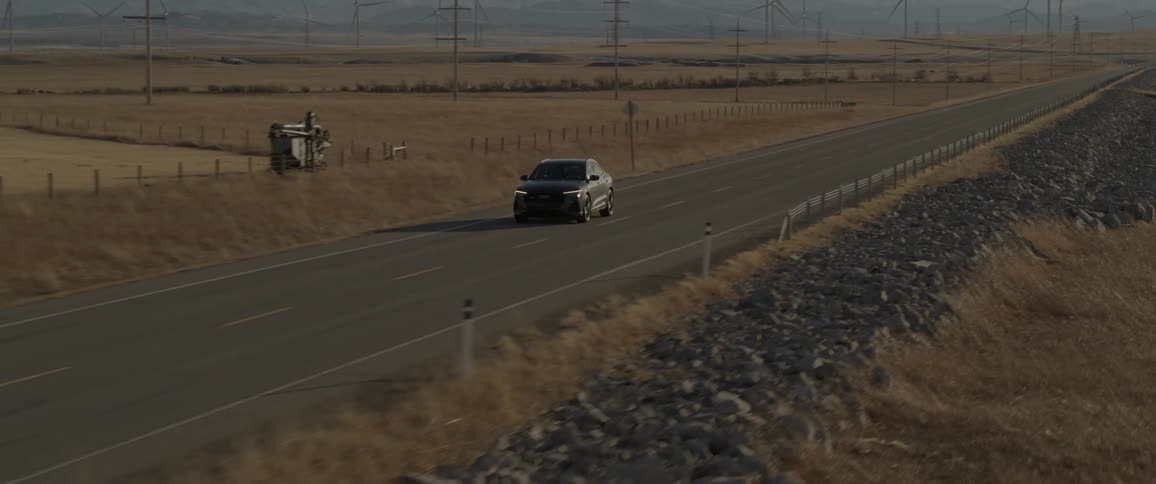 An automobile speeds along a paved road that passes through a rural area