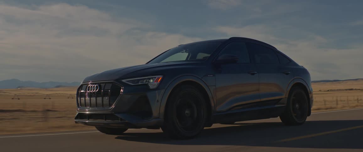 A black audi car travels on a country road under a cloudy sky