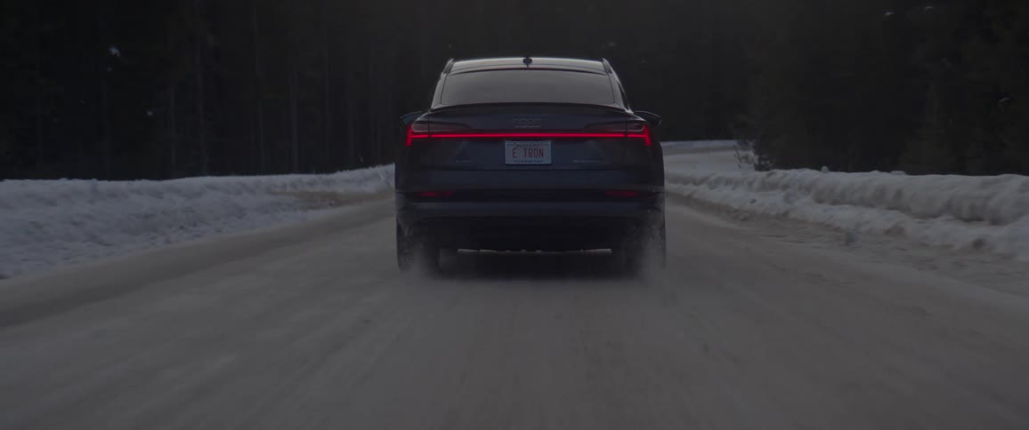 Dark grey audi car drives on snowy dirt road in the forest