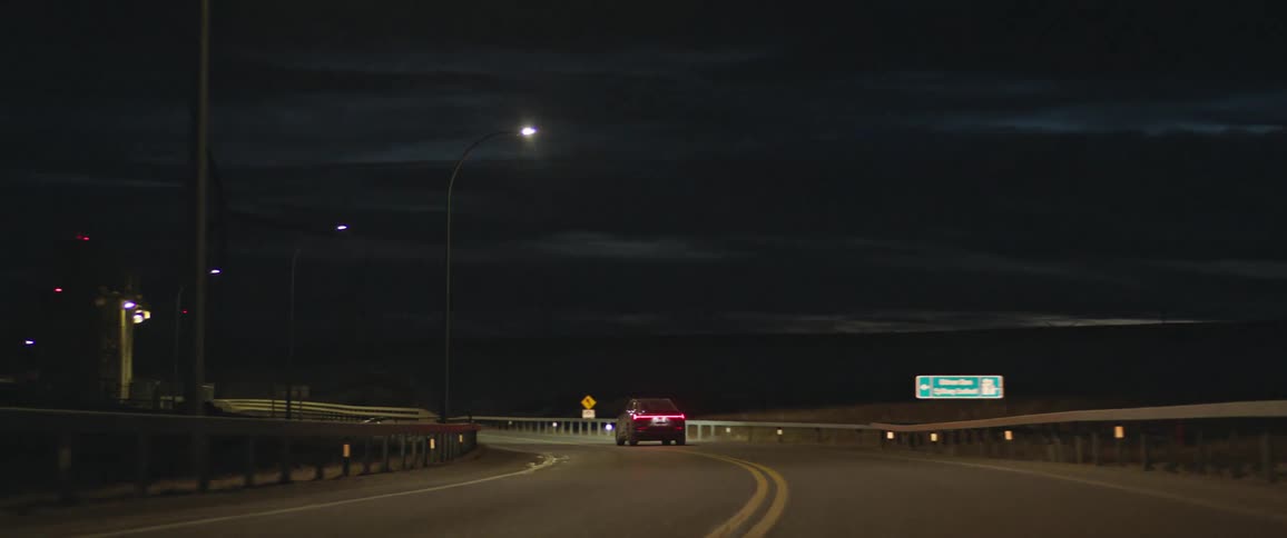 A vehicle drives past bright street lamps on a rural highway at night