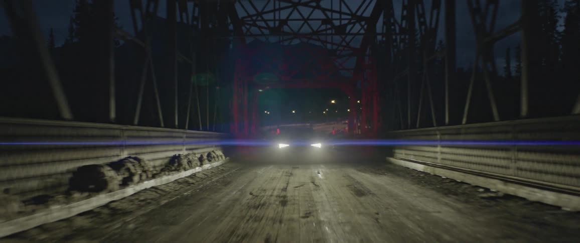 Dark grey audi illuminating the road with headlights drives across a bridge at night