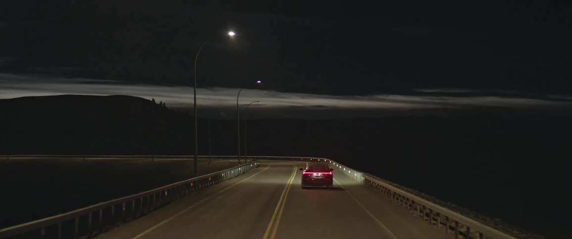 A vehicle drives with bright headlights on down a rural highway at night