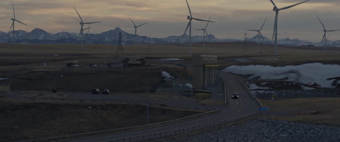 A vehicle driving on a road with wind turbines the sky and clouds in the background