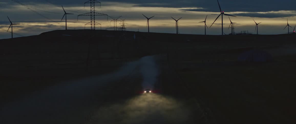 A car driving down a dirt road near a windmill