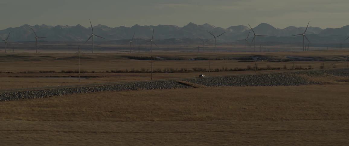 Car driving on a rural road near a wind farm on the plains close to the mountains at morning