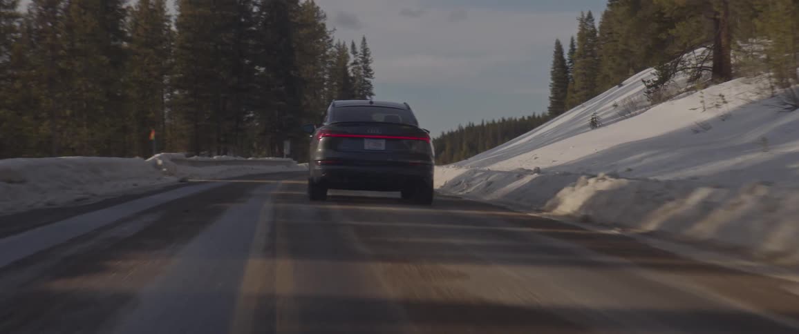 Dark grey audi car drives uphill on the snowy forest road