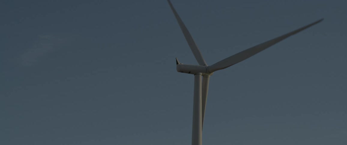 A wind turbine is spinning with few clouds in the sky