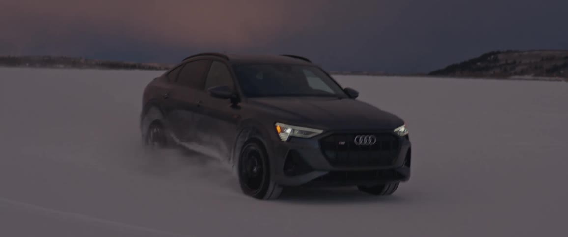 A car driving on a snowy field with a mountain range the sky and clouds in the background