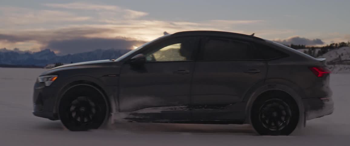 A black car travels through the snow as the sun is setting