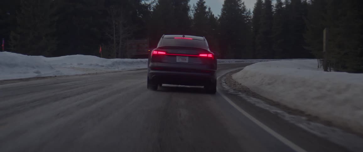 A black car travels on a road with the left blinker flashing before it turns