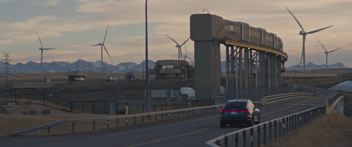 Black car driving over a bridge near a wind farm at sunset