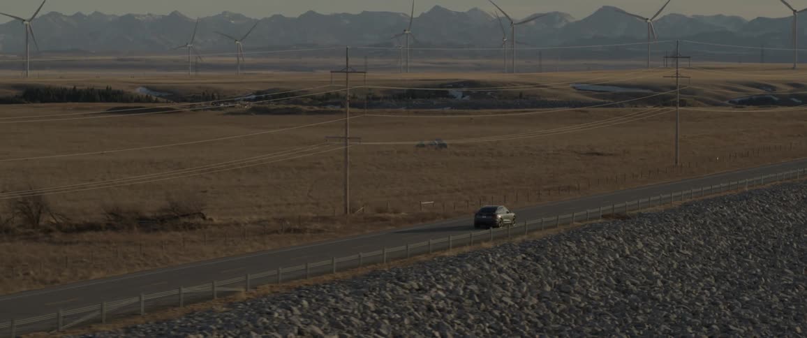 Black car driving on a road near a wind turbine farm on he countryside at morning