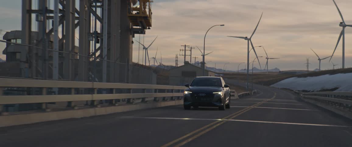 A vehicle driving on a road with wind turbines the sky and clouds in the background