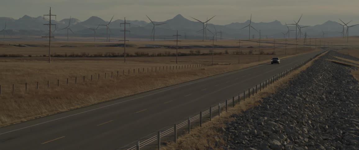 Dark gray audi car drives on highway next to wind farm