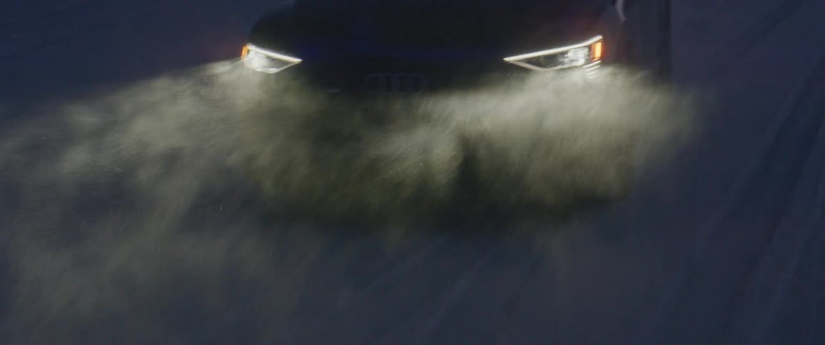 A vehicle with headlights driving on a snowy field