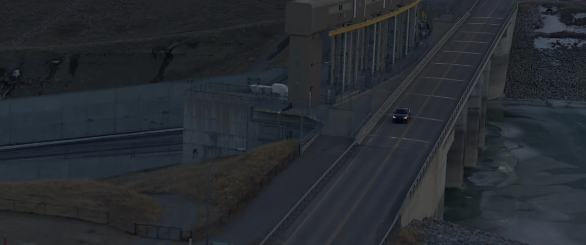 An aerial view of a car traveling on a lonely highway over a waterway at dusk