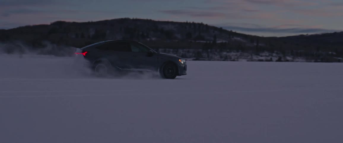 Black car driving on a snow covered desert near the mountains at morning