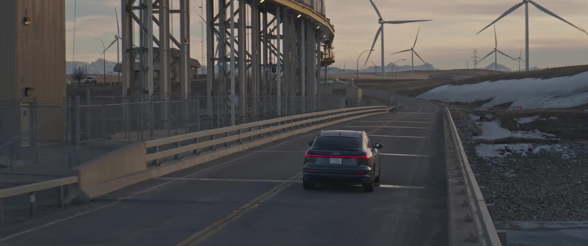 A car is driving on a rural highway at dusk