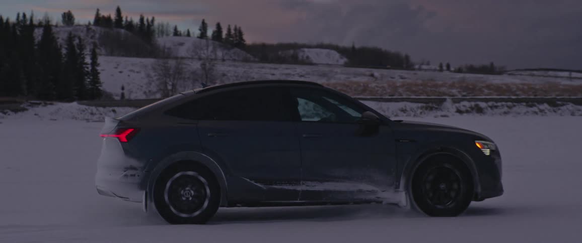 A vehicle driving on a snowy field with trees the sky and clouds in the background