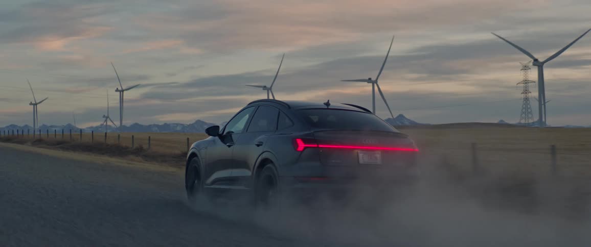 A black car travels on a road with spinning wind turbines along the roadside