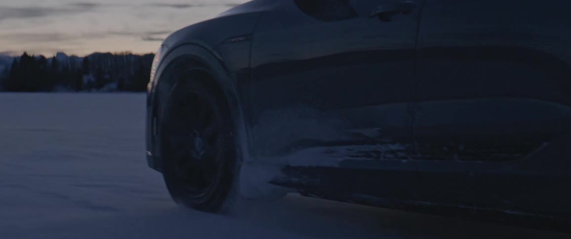 A car is driving on a road in winter at dusk