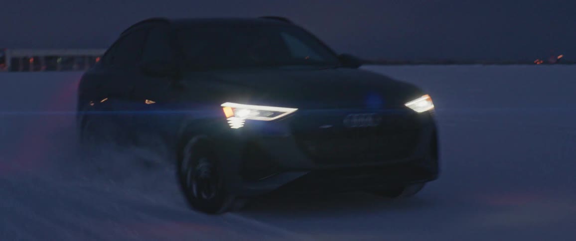Dark grey audi car drives in the snowy field at dusk