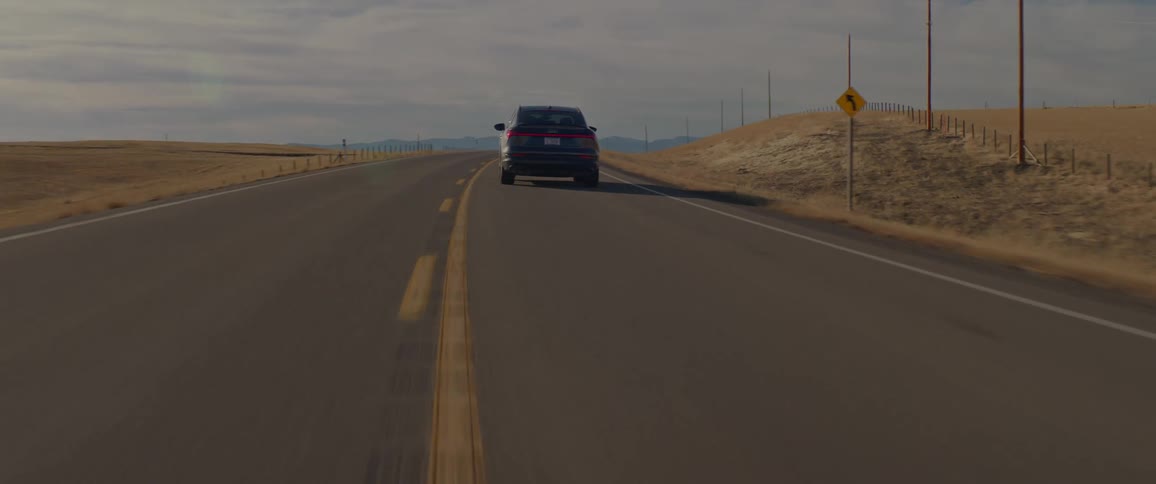 A black car is driving on a road with desert on both sides