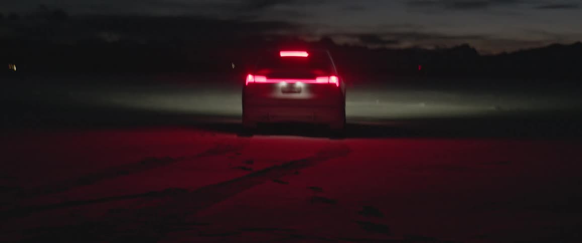 A car sits on the soil facing hills and a dark sky