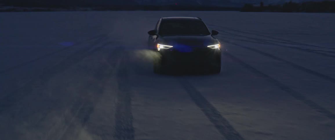 A black car with headlights on travels on a snow covered road