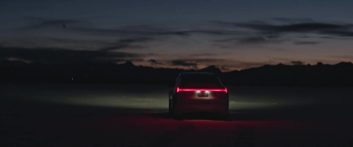 Red brake lights on a car parked on a desert at sunset