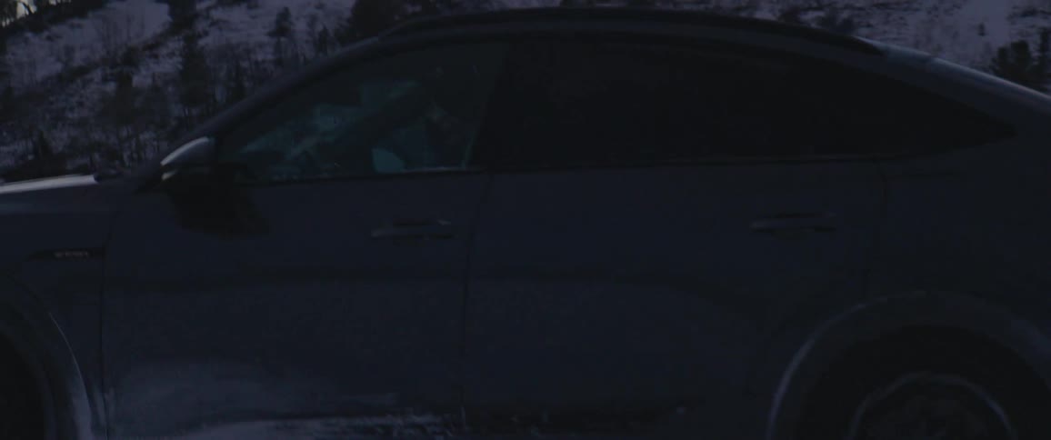 Audi car drives in the snowy field with hills in the backgound at dusk