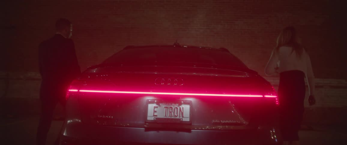 A man and a woman holding hands and getting into a car with a wall in the background