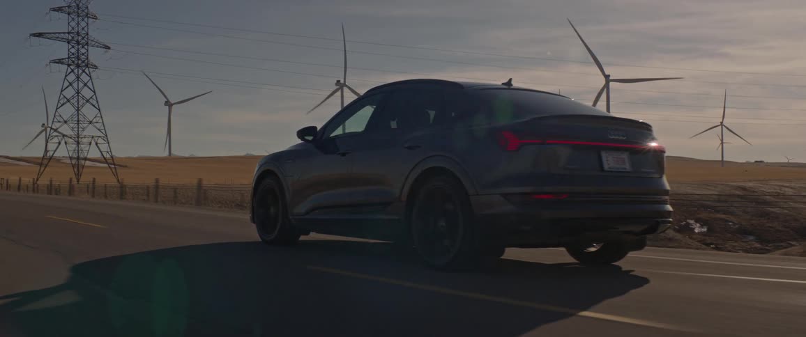 A vehicle driving on a road with wind turbines the sky and clouds in the background