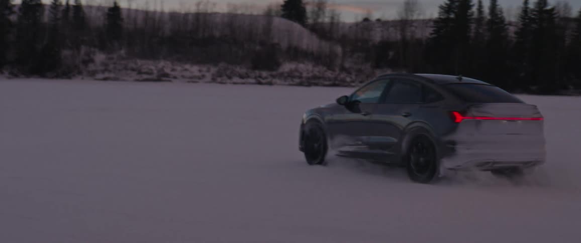 Black car driving on a snow covered desert near the mountains at morning