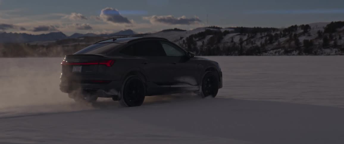 Black car driving on a snow covered desert near the mountains at morning