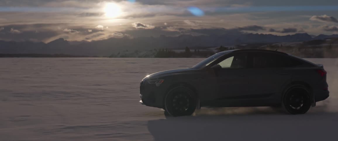 Side view of dark grey audi car driving across the snowy field