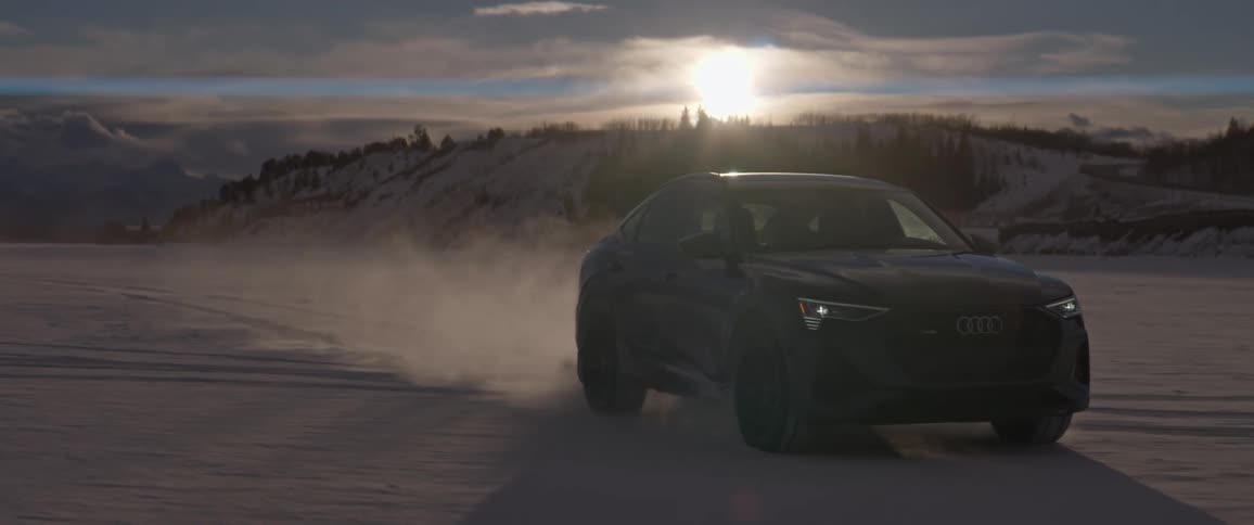 A car travels along an open desert terrain with a mountain hill in the background