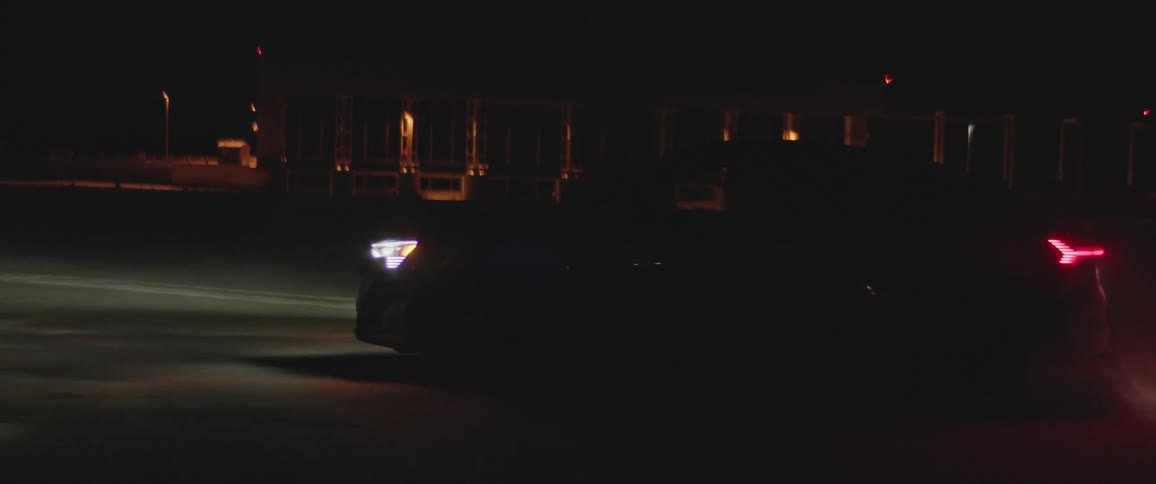 Black sports car with headlights on driving near a bridge in the countryside at night