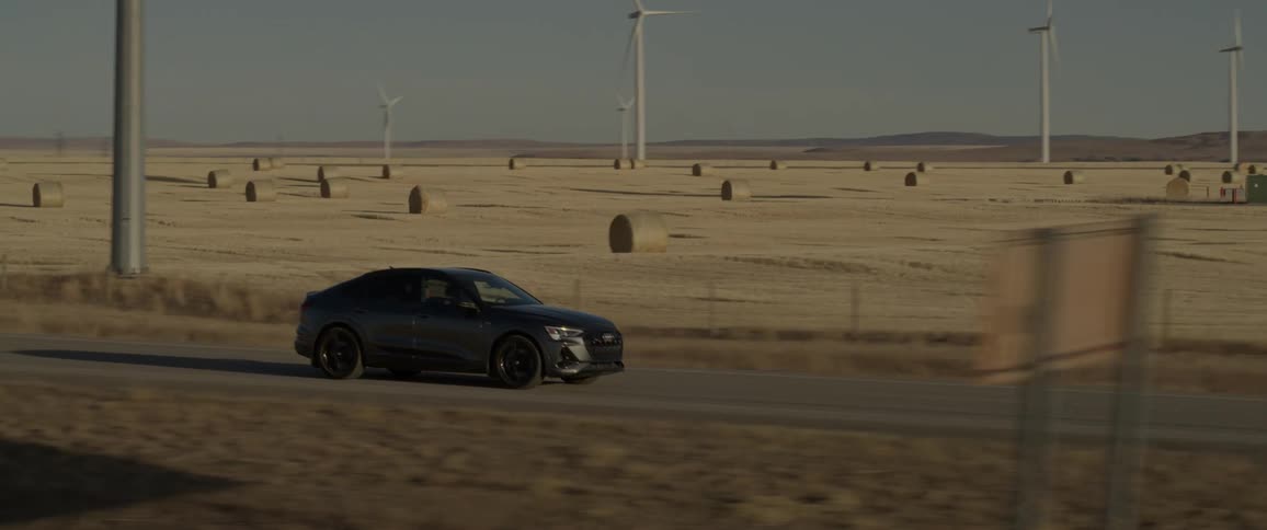 A vehicle drives along a rural road beside wind turbines
