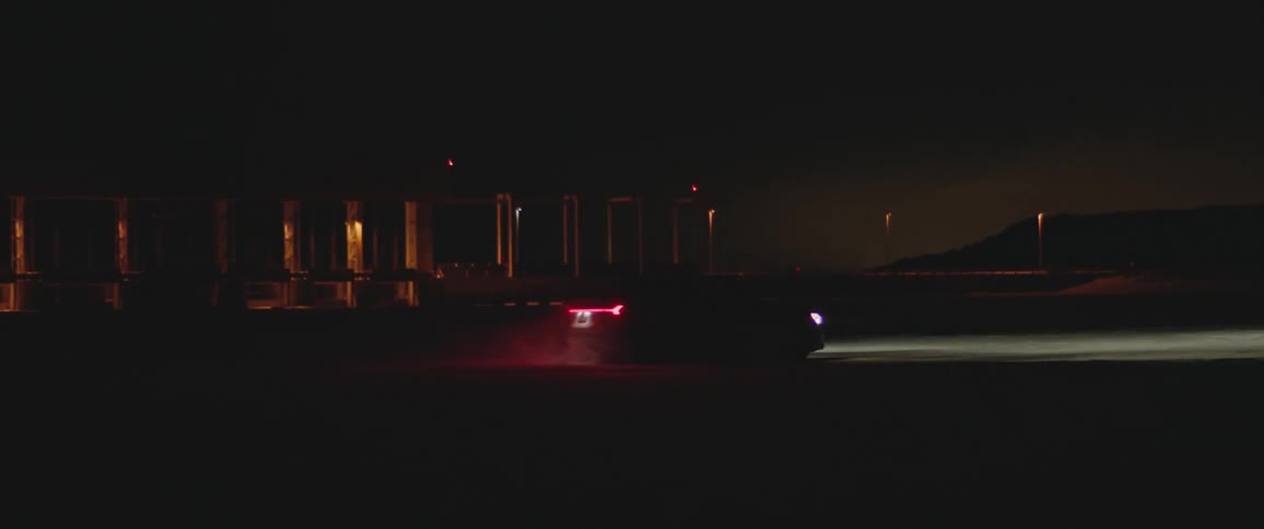 Black sports car with headlights on driving on the snow covered plains near a bridge at night