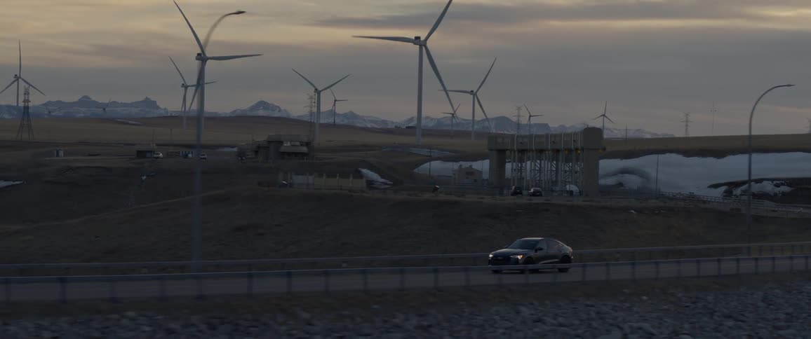 A car travels on a road surrounded by spinning wind turbines