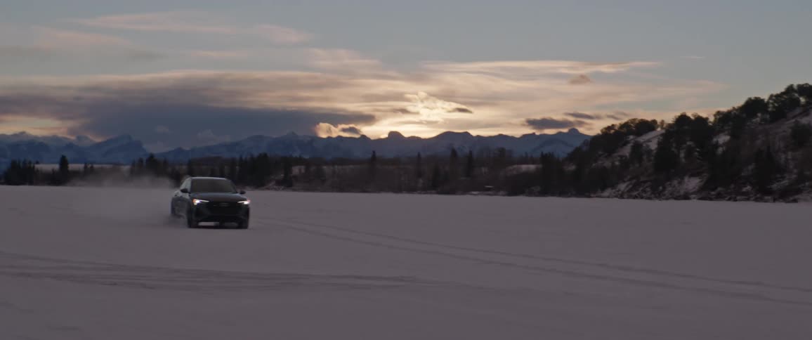 Black car driving on a snow covered desert near the mountains at morning