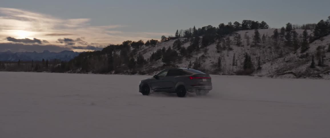 A black car travels through the snow as the sun is setting