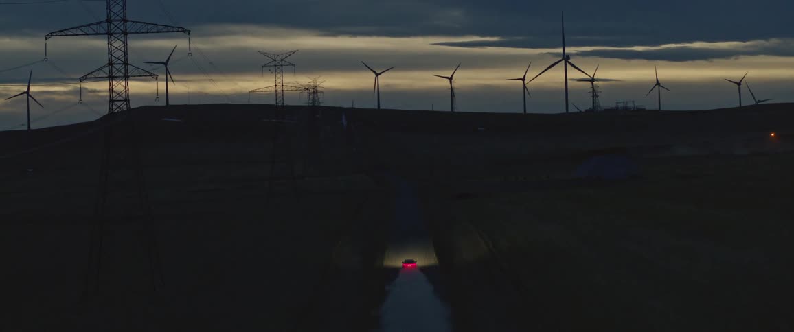 A car is driving on a free while you can see multiple windmills at a distance