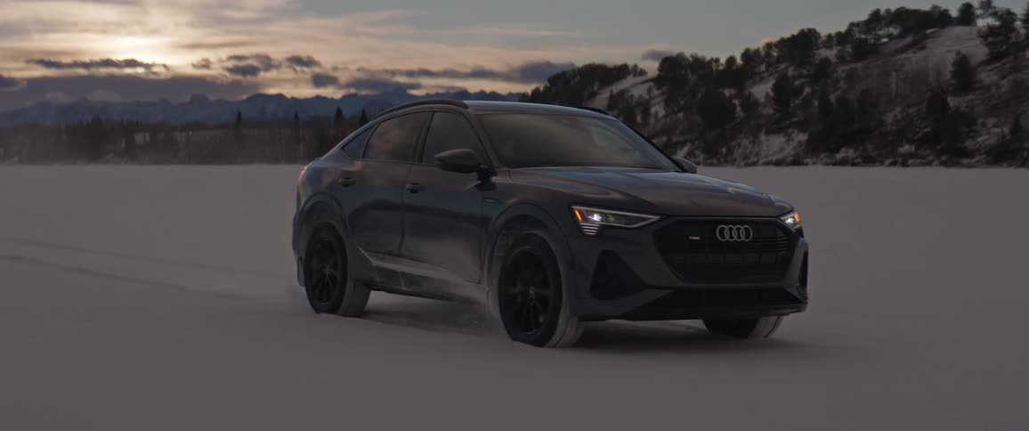 Black car driving on a snow covered desert near the mountains at morning